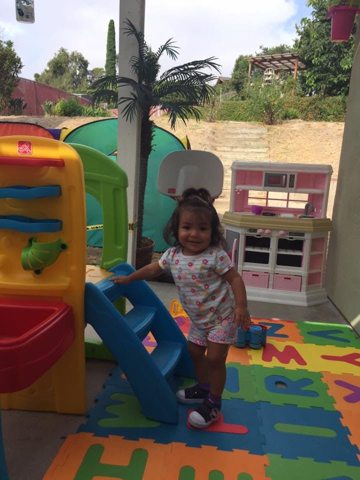 Child standing next to a blue slide on a colorful alphabet mat