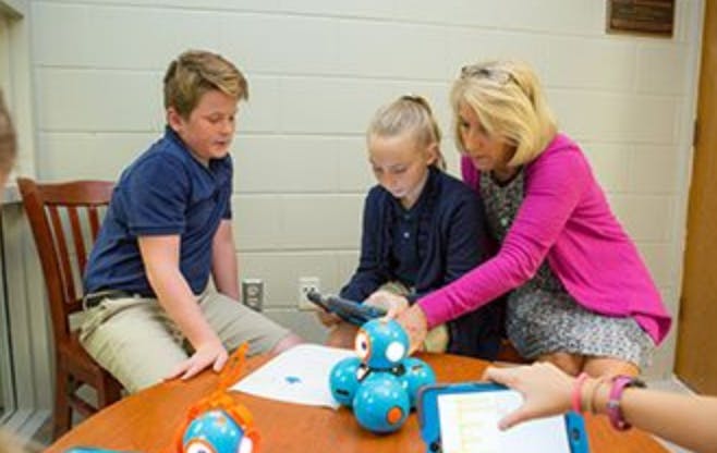 Adult and two children interacting with a robot and tablets