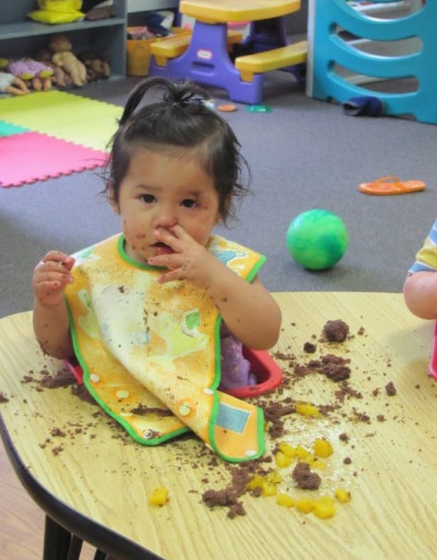 Child in a bib with food on their face and on a table