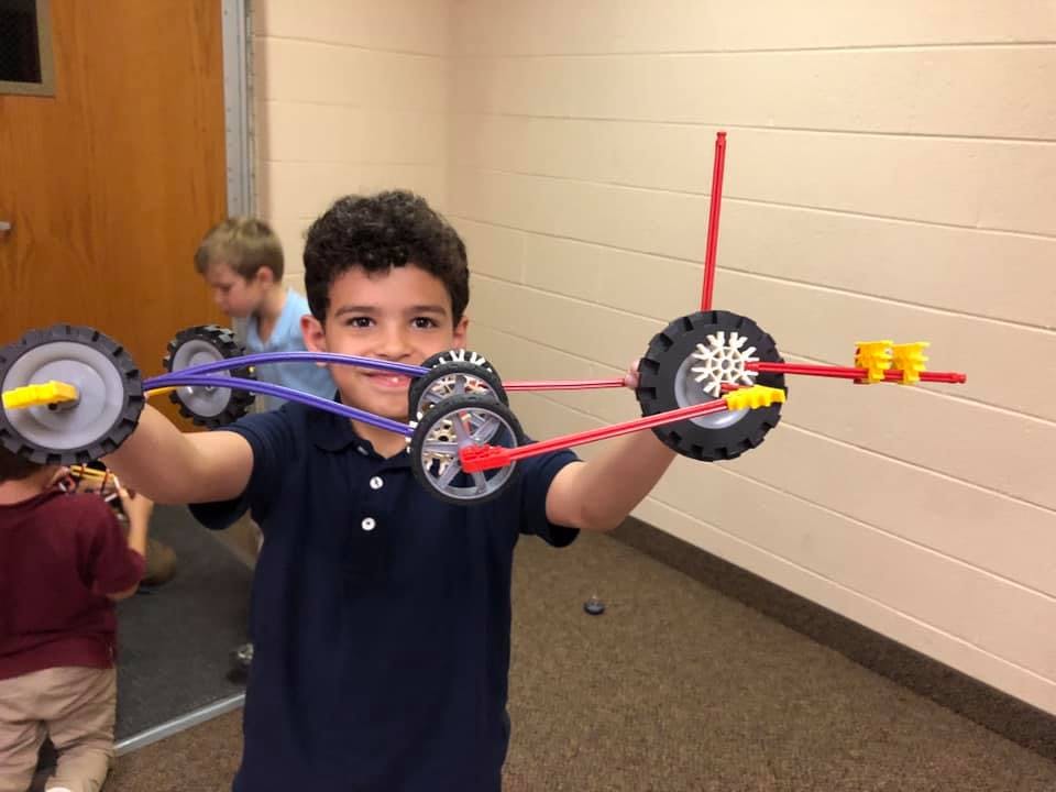 Child holding up a toy made of wheels and colorful rods