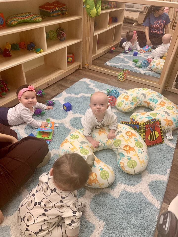 Three babies on a rug with toys and pillows