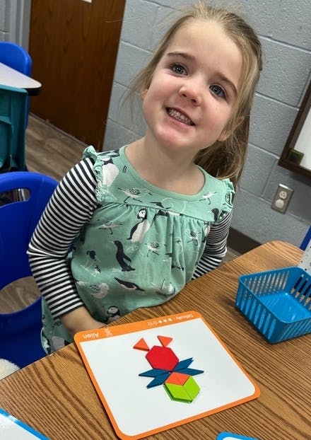 Child smiling at a table with a colorful geometric puzzle