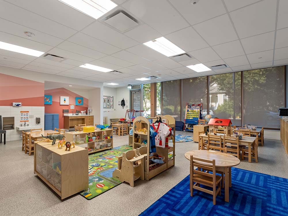 Empty colorful children's classroom with small tables, chairs, and play areas