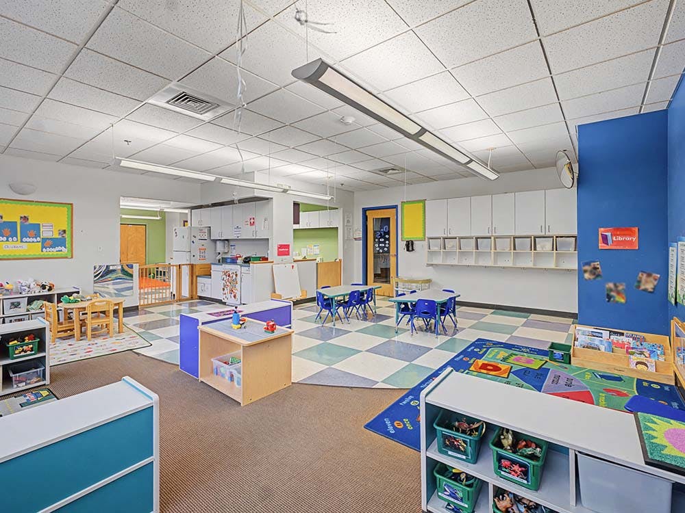 Classroom with small tables and chairs, play mats, and storage units