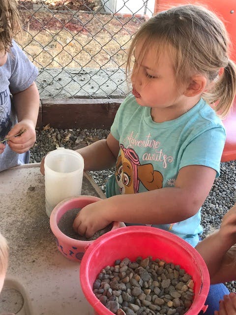 Child playing with sand and rocks in bowls