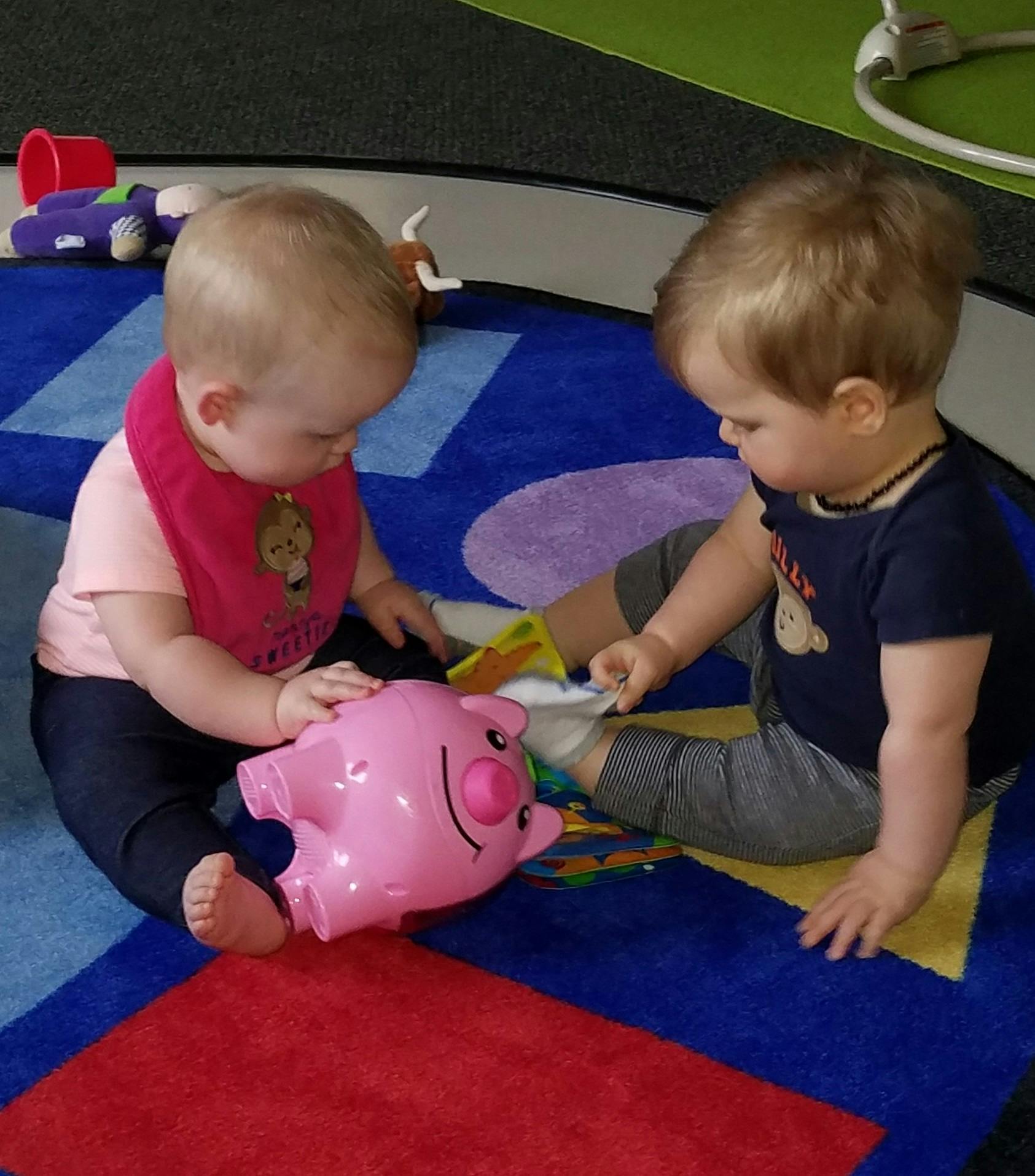 Two children playing with a pink toy pig on a colorful rug