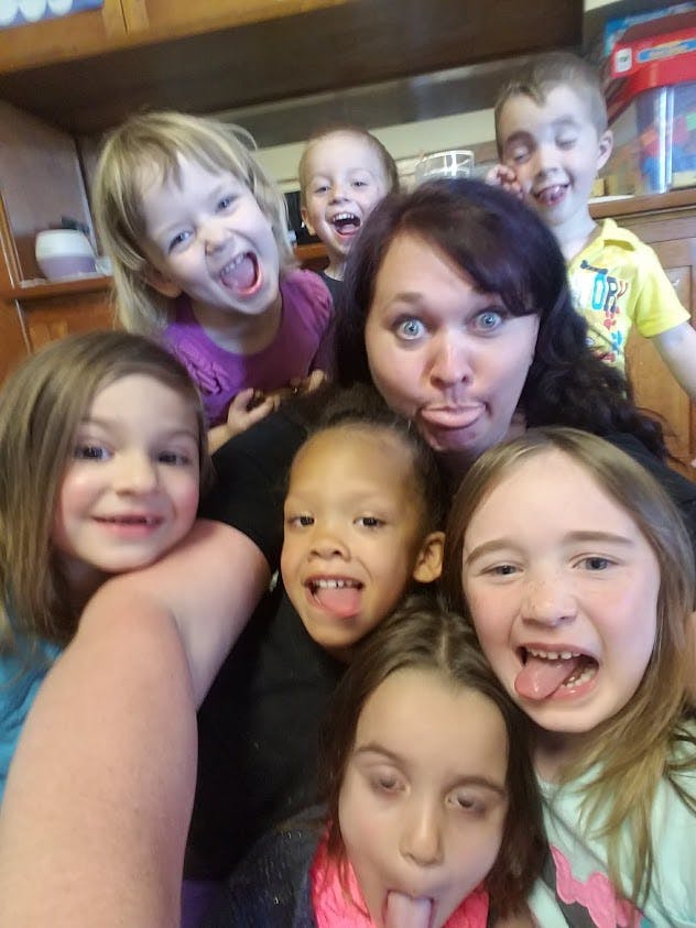 One adult and multiple children making funny faces and sticking out tongues