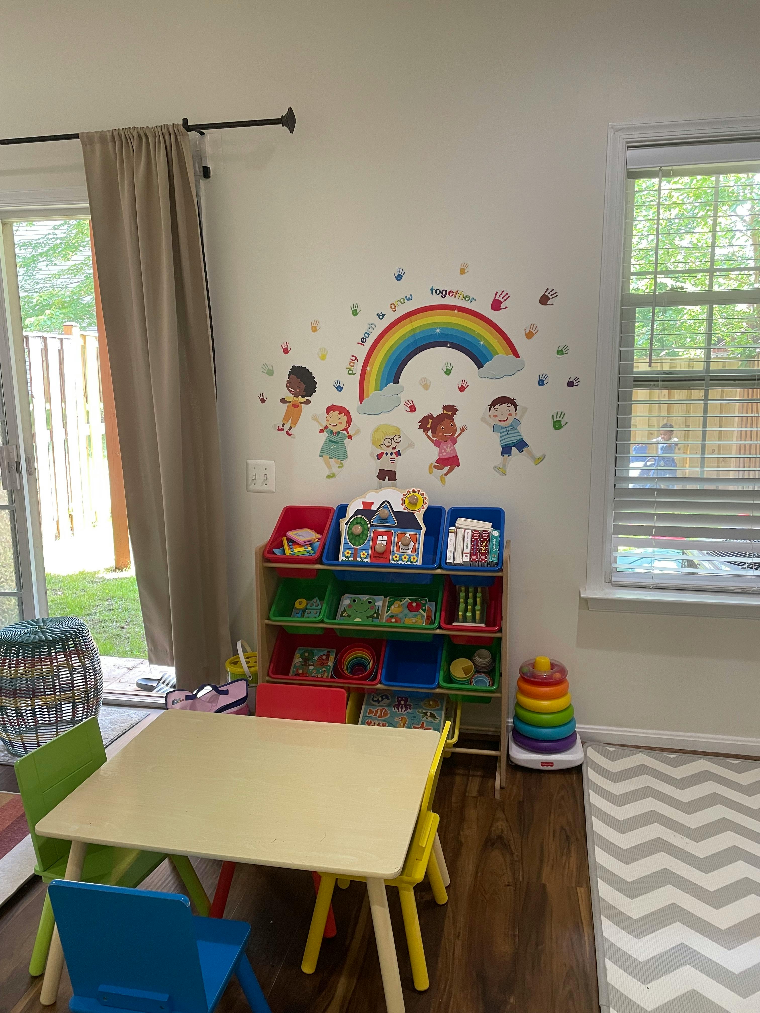 Children's play area with a table, chairs, toy organizer, and rainbow wall decal