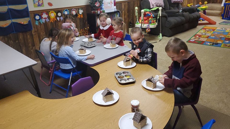 Children decorating small gingerbread houses at tables