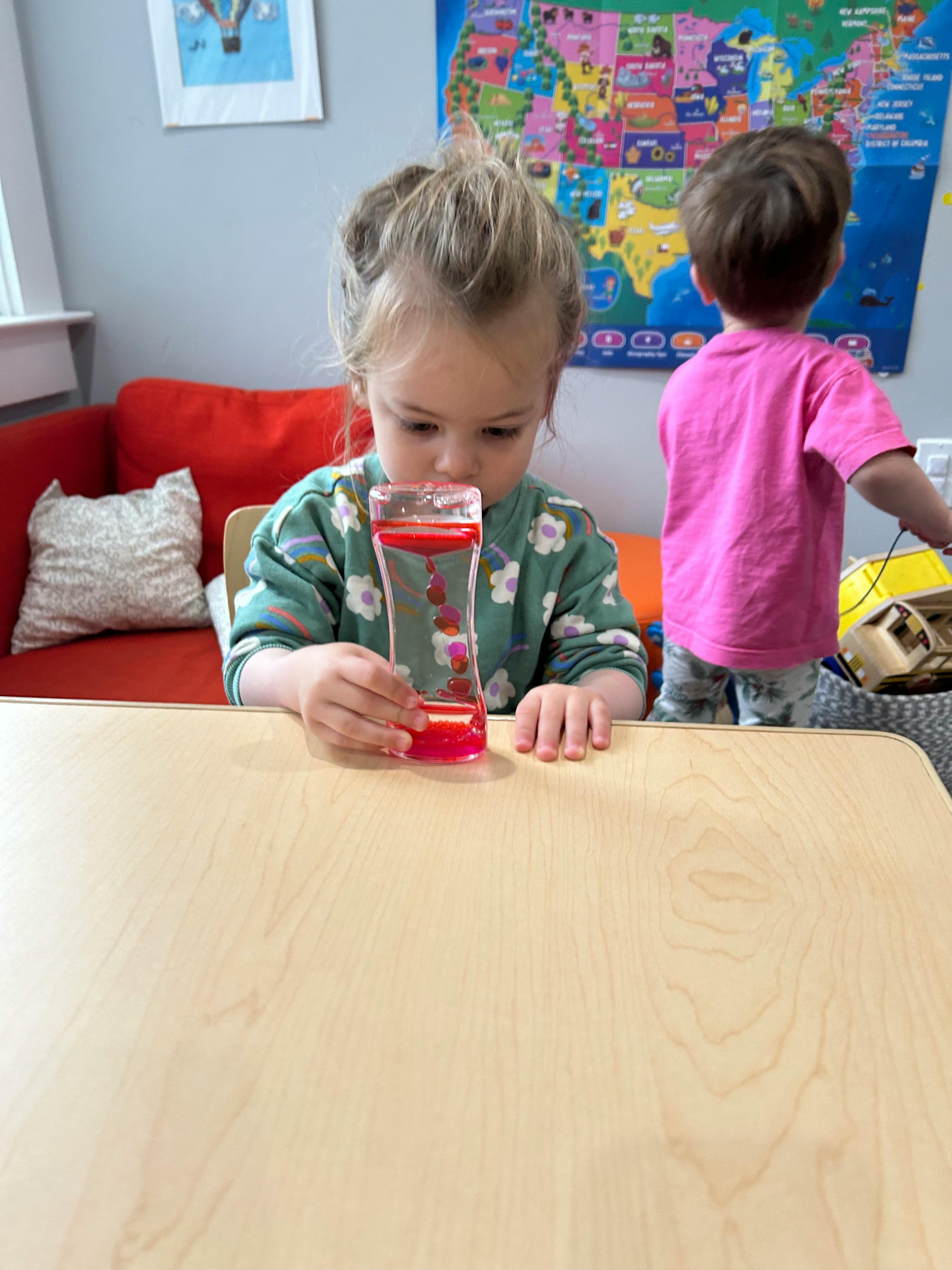 Child holding a liquid motion timer at a table