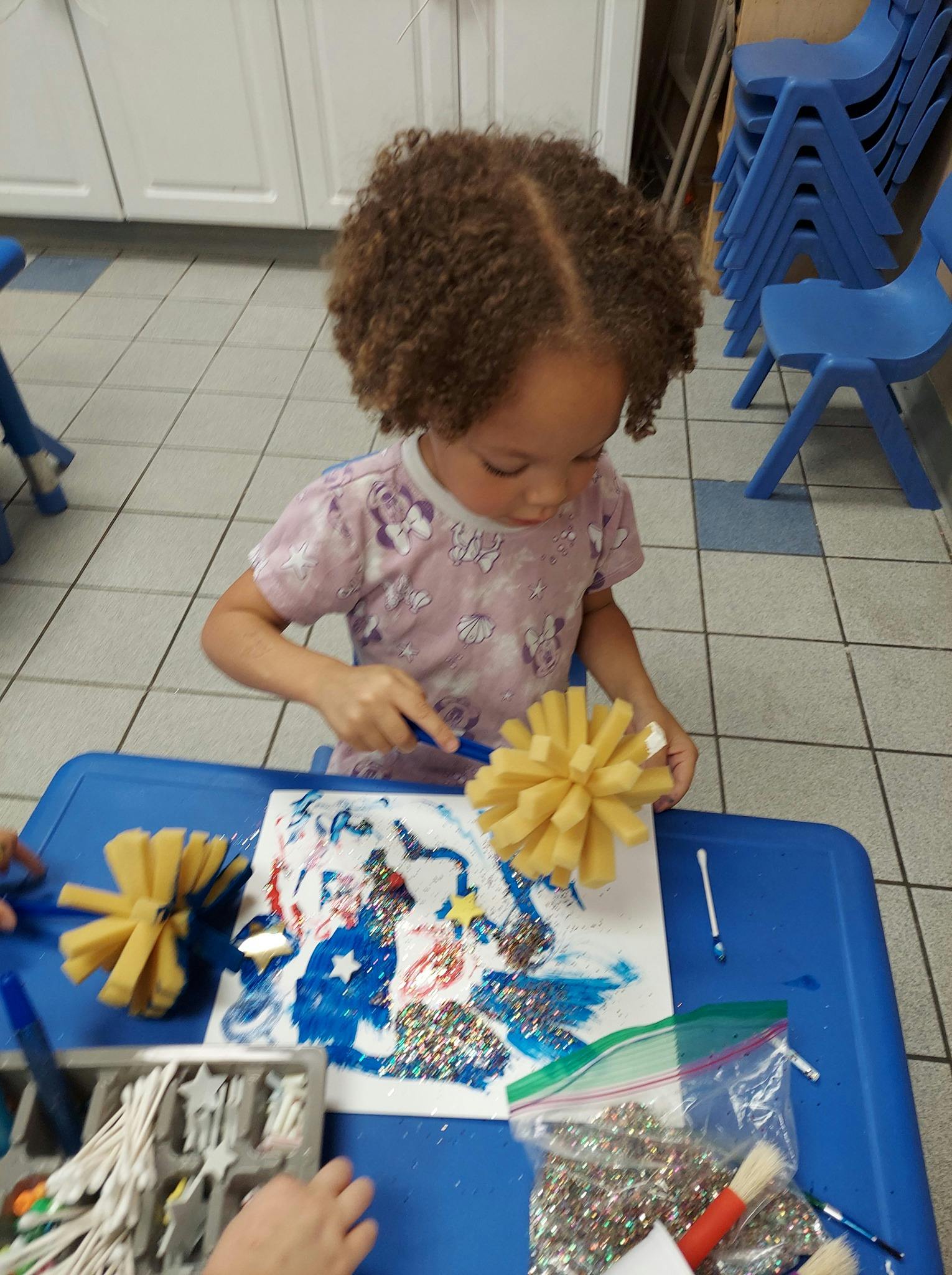 Child painting with a sponge on a blue table