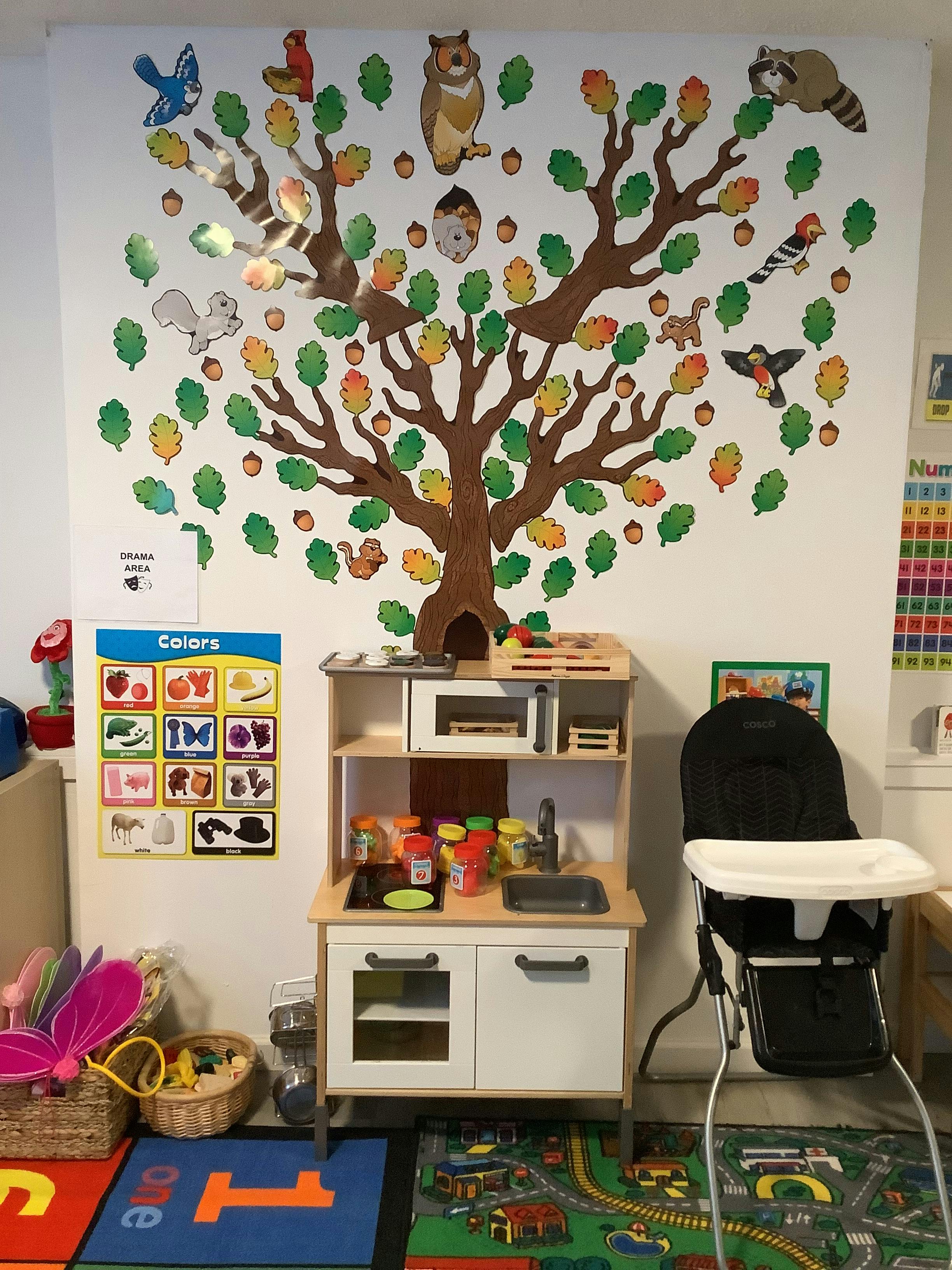 Play kitchen with a high chair and a tree wall decal with animals