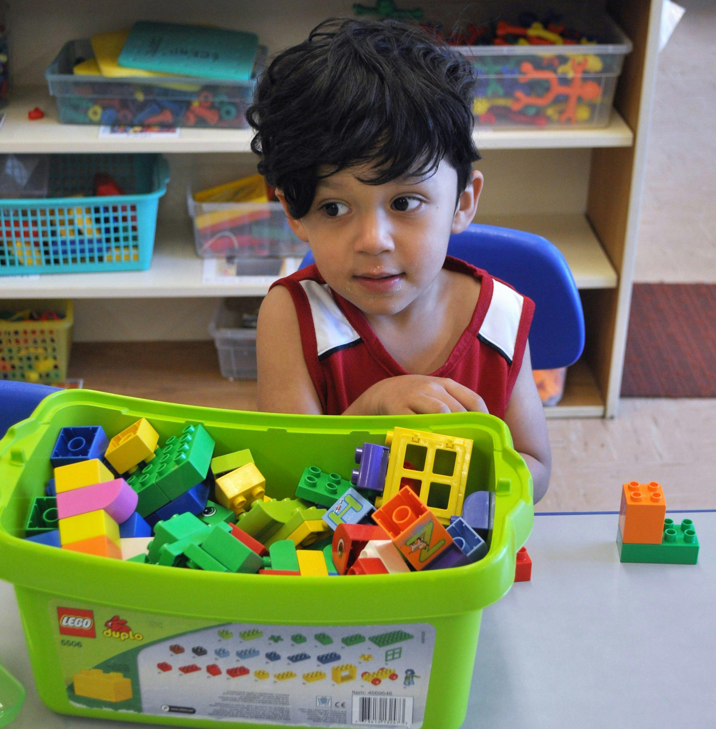 Child sitting at a table with a bin of building blocks