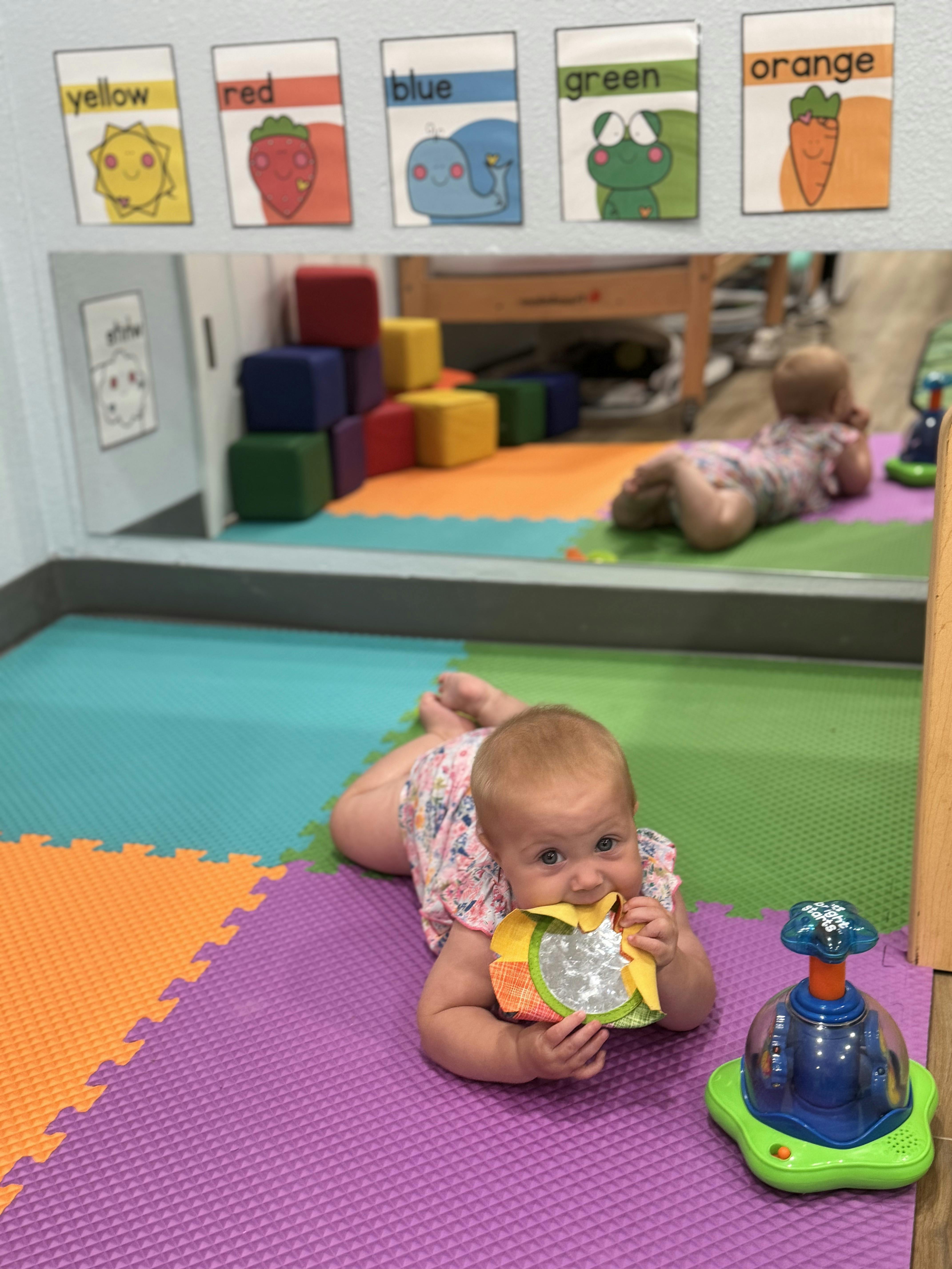 Child on colorful mat playing with a toy, reflection in mirror