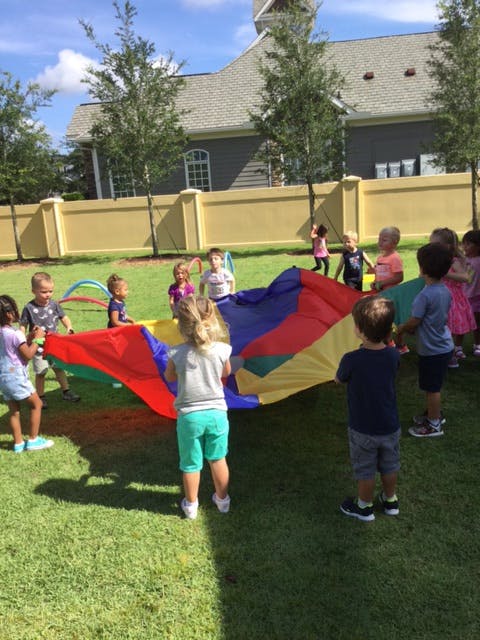 Children playing with a colorful parachute on a grassy lawn