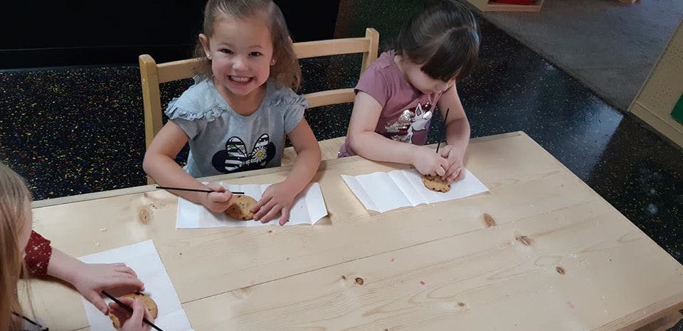 Children painting small objects at a table