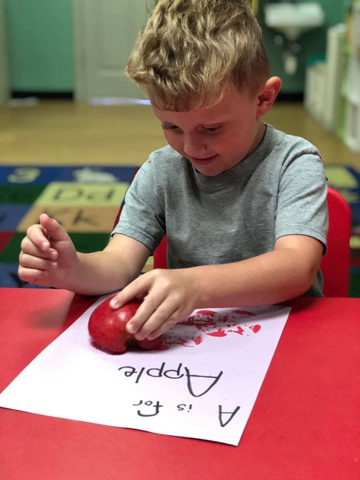 Child making apple prints on paper with "A is for Apple" written on it