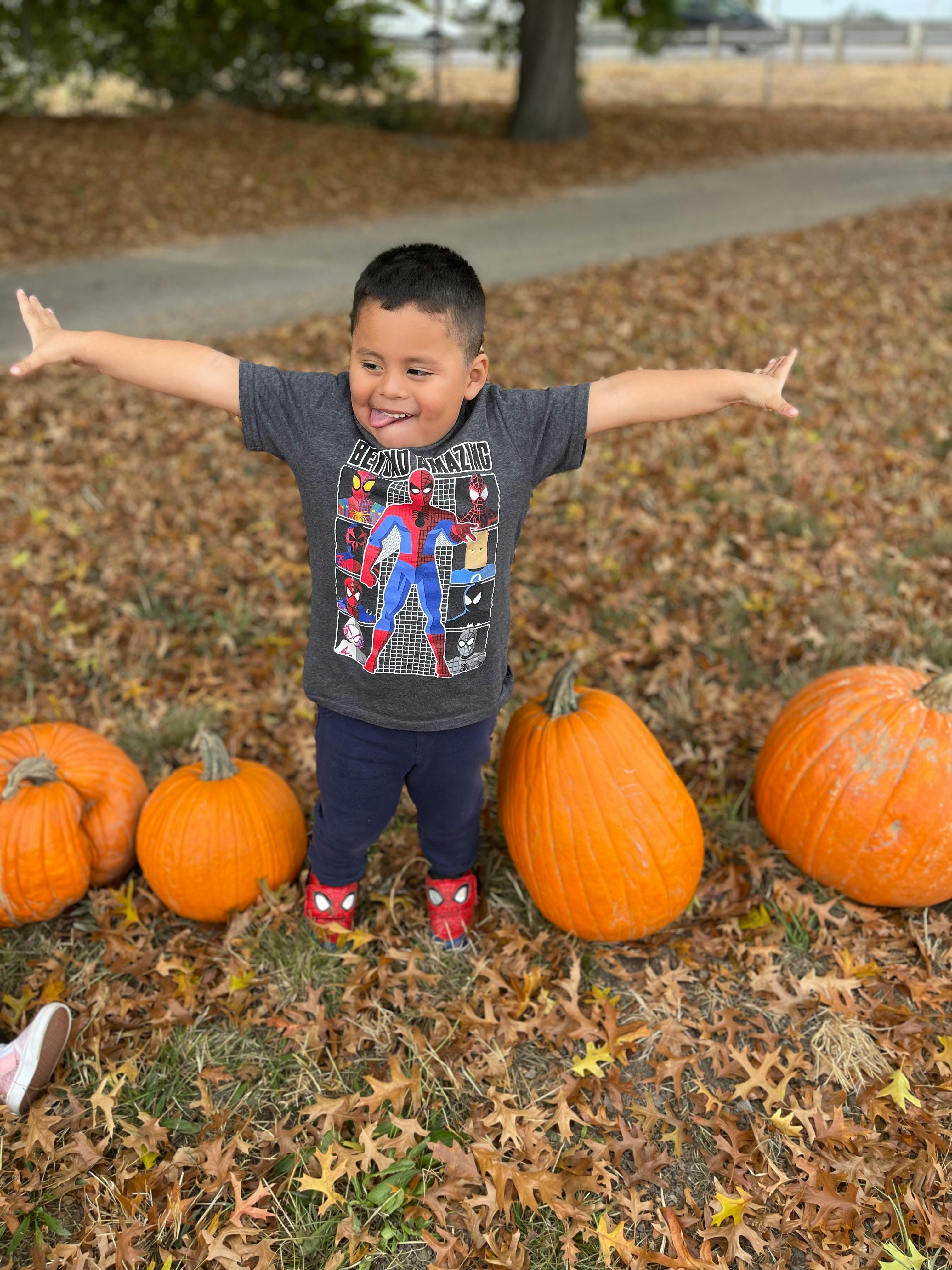 Child standing with arms outstretched among pumpkins and fallen leaves