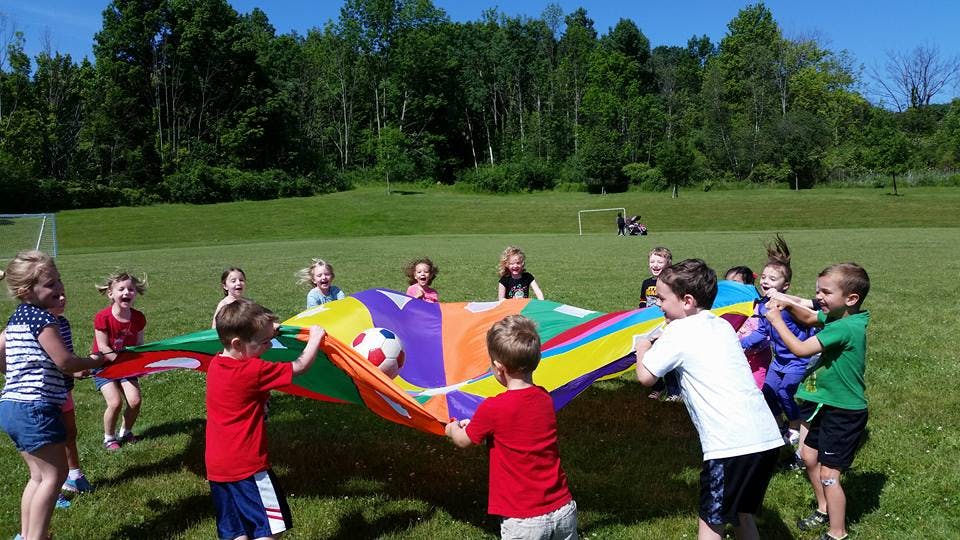 Children playing with a colorful parachute and a ball outdoors