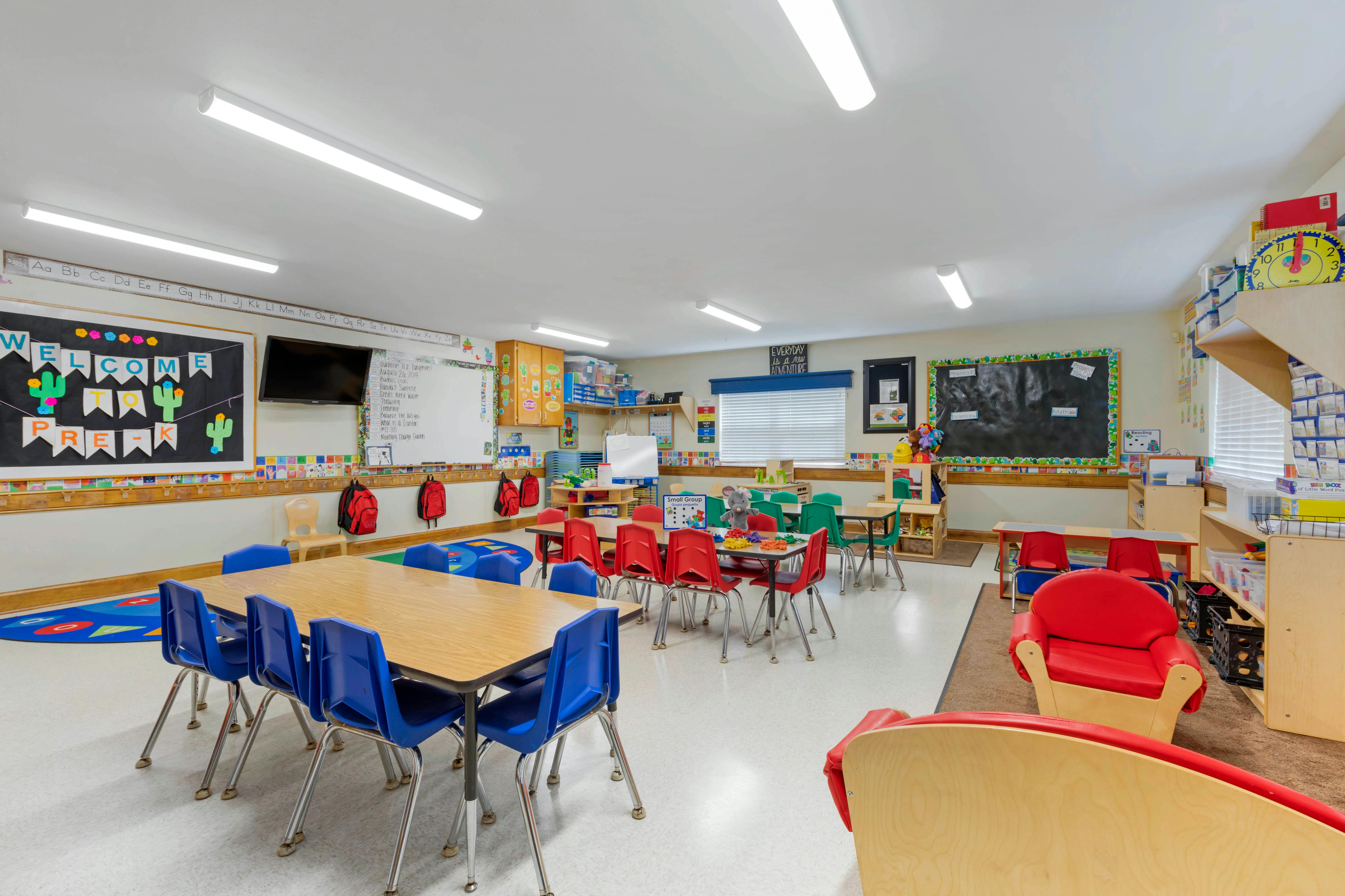 Classroom with multiple tables and chairs, whiteboards, and children's decorations