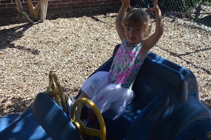 Child sitting in a toy car with arms raised