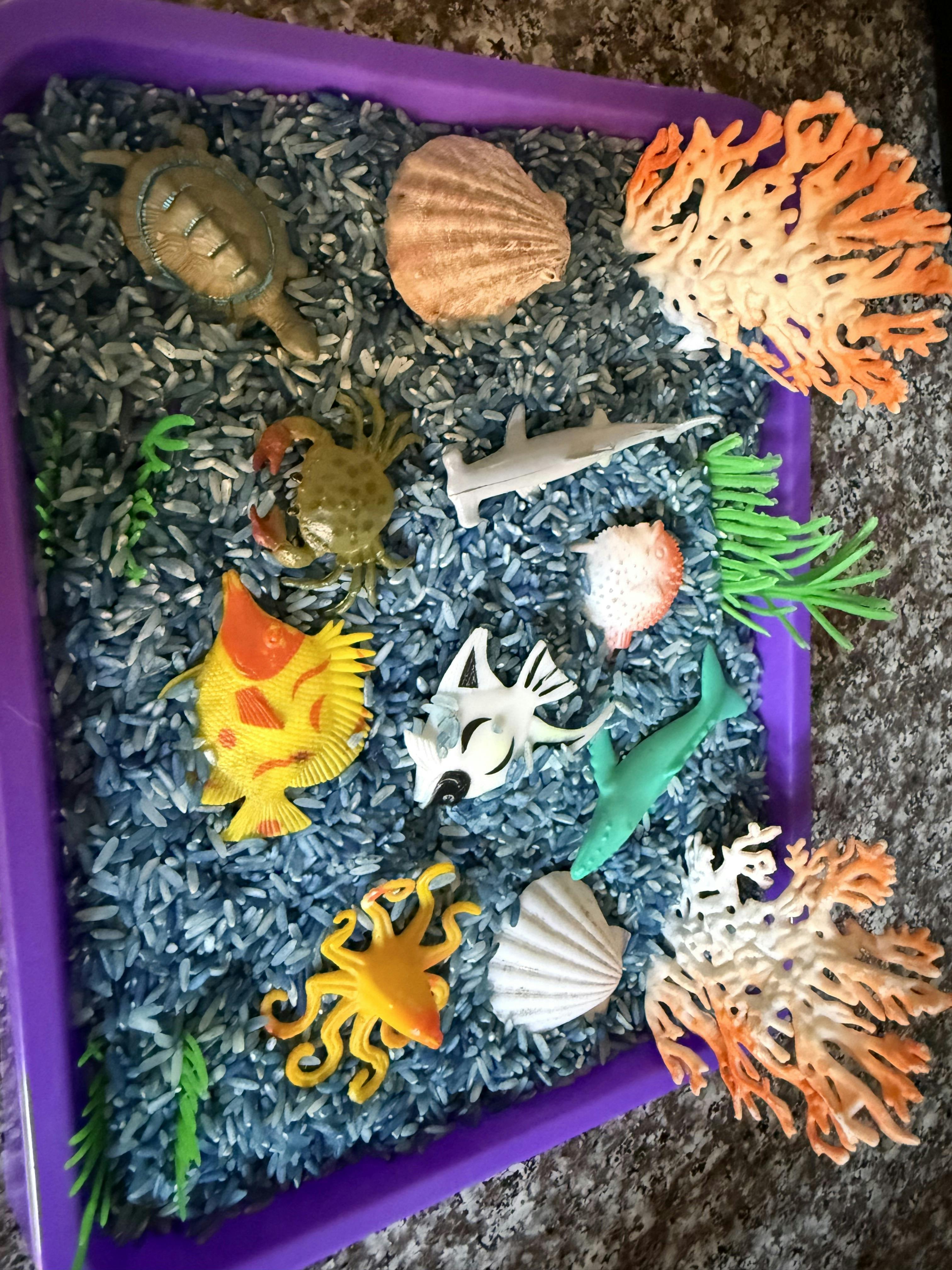 Plastic sea animal figures and coral in a tray of blue rice