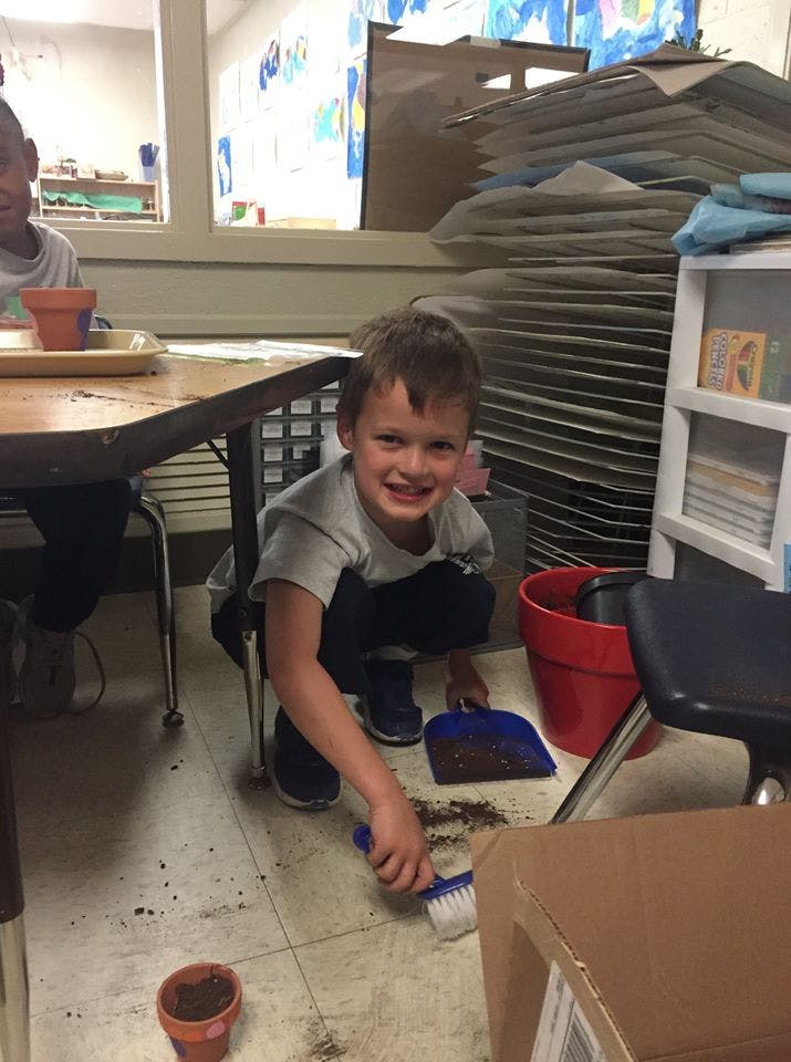 Child sweeping dirt into a dustpan on the floor