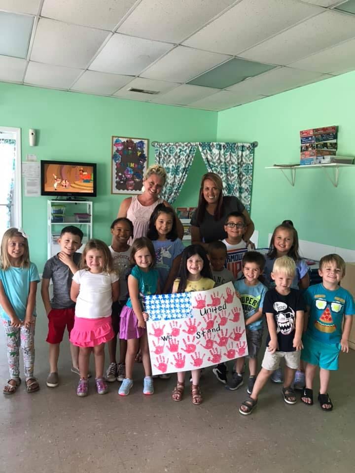 Two adults and a group of children holding a sign with handprints and text