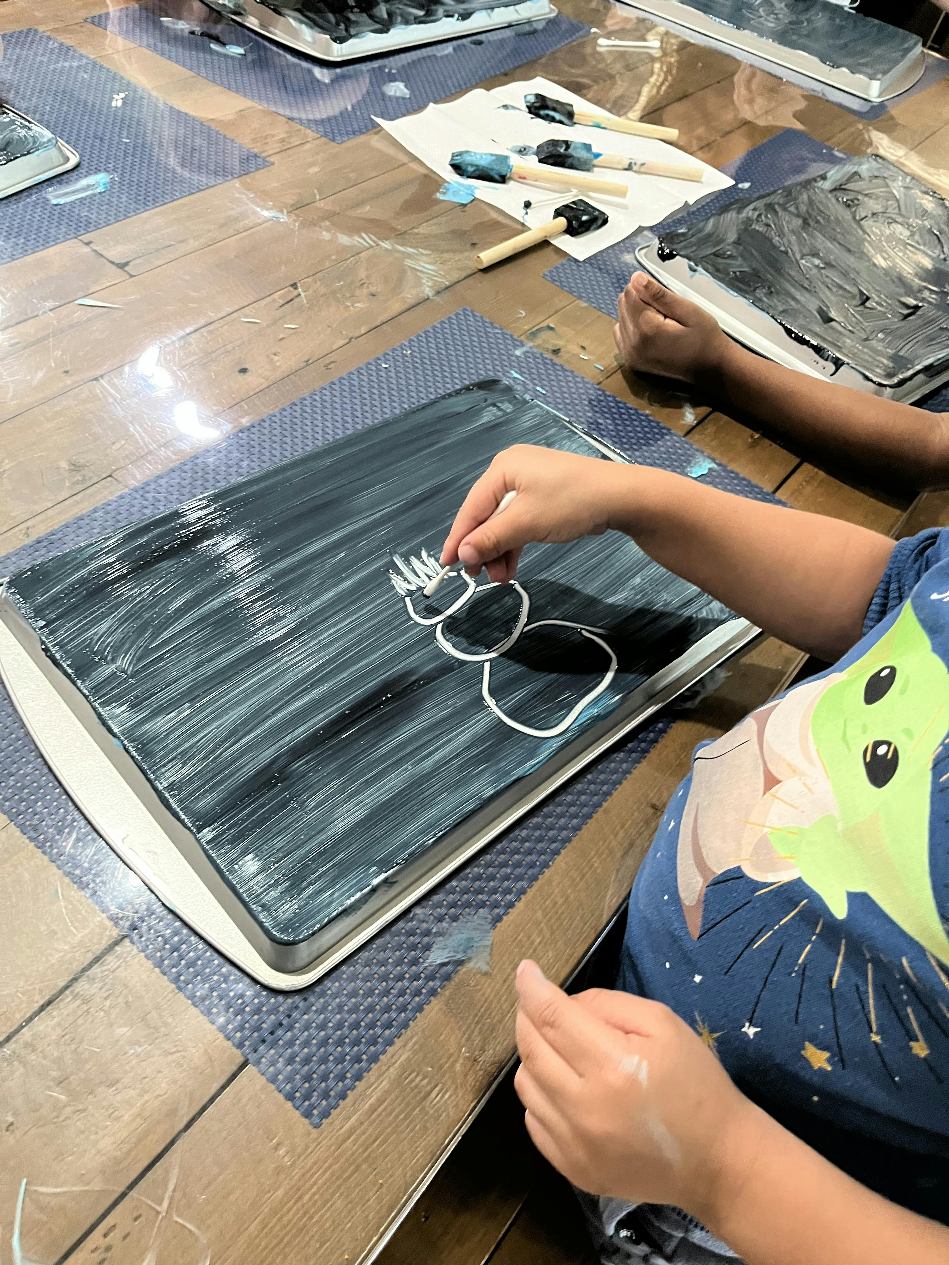Child drawing a snowman on a black painted surface