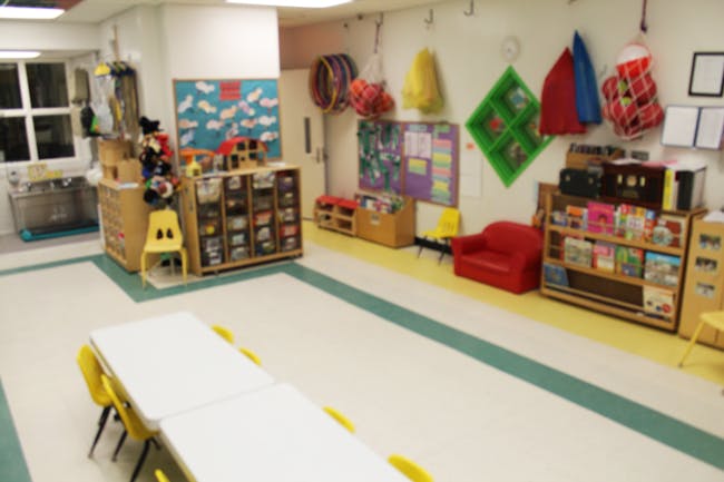 Empty classroom with tables, chairs, and shelves of books and toys