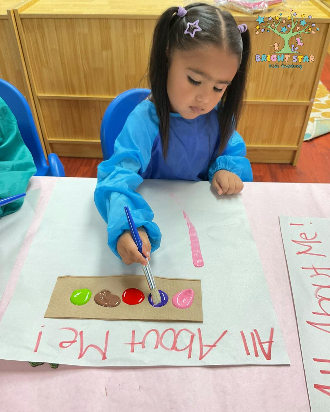 Child painting with various colors on paper with "All About Me!" written on paper