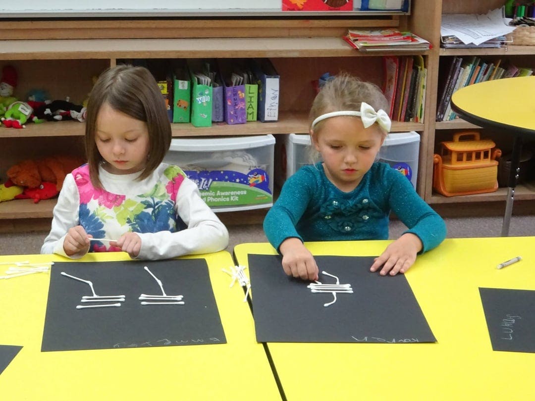 Two children creating art with cotton swabs on black paper