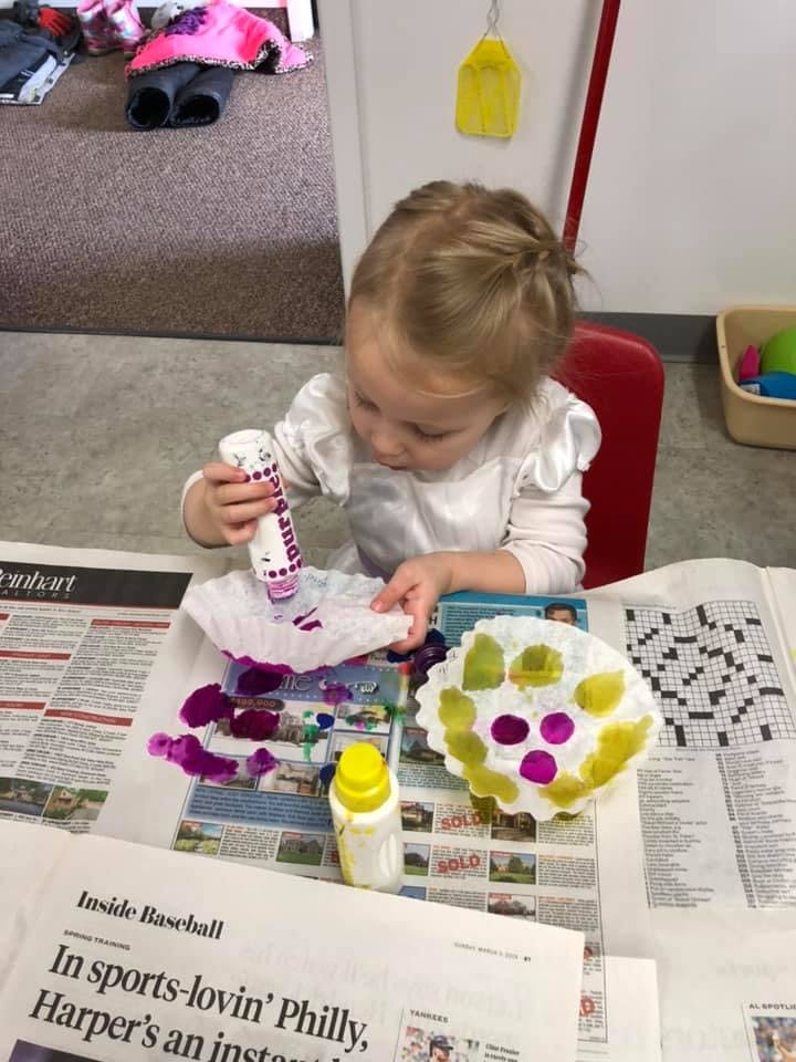 Child painting a paper coffee filter with purple paint