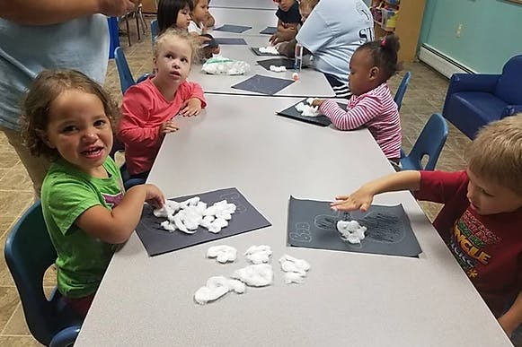 Children at a table doing an art activity with white material on black paper