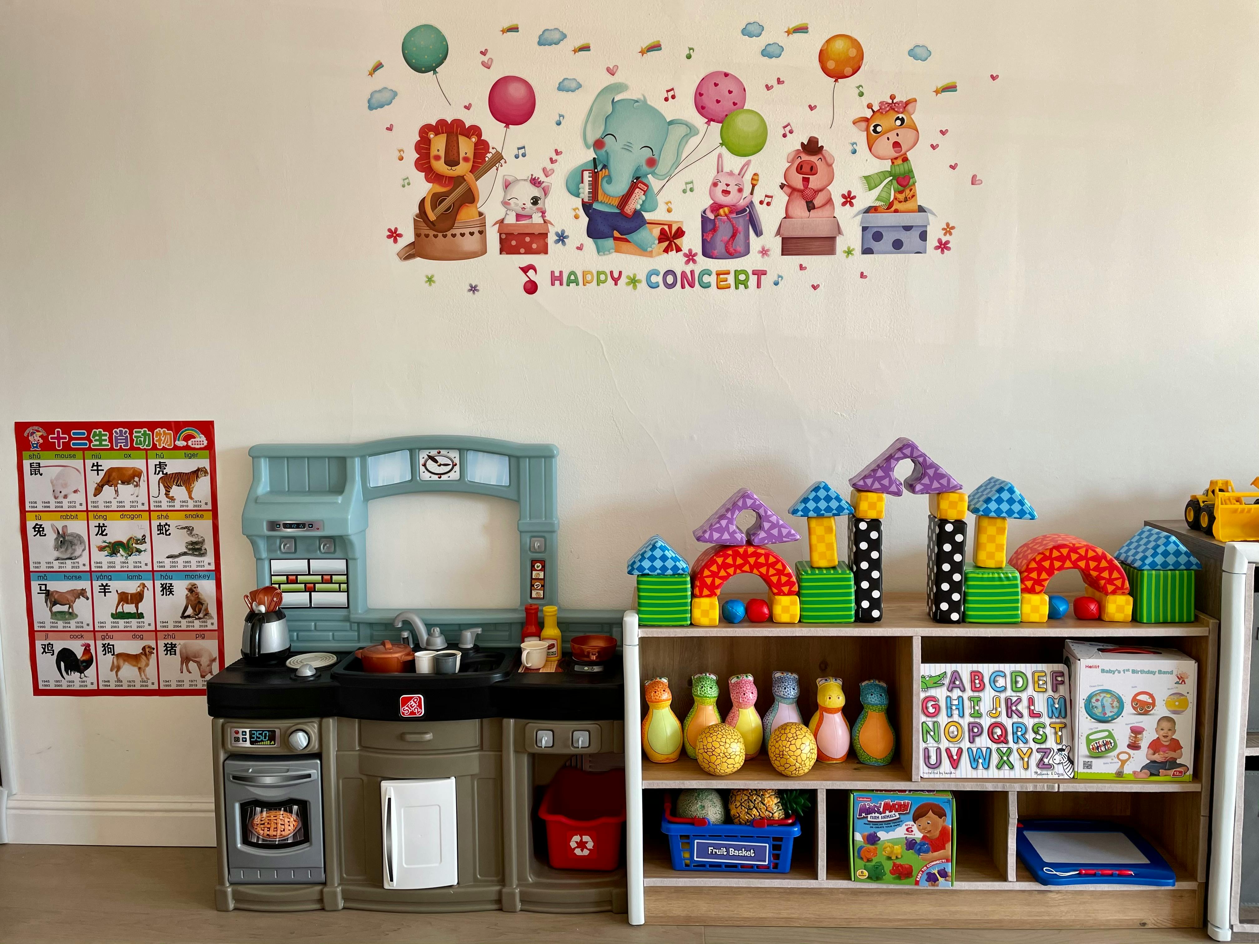Play kitchen and shelves with toys in a room with a wall decal above