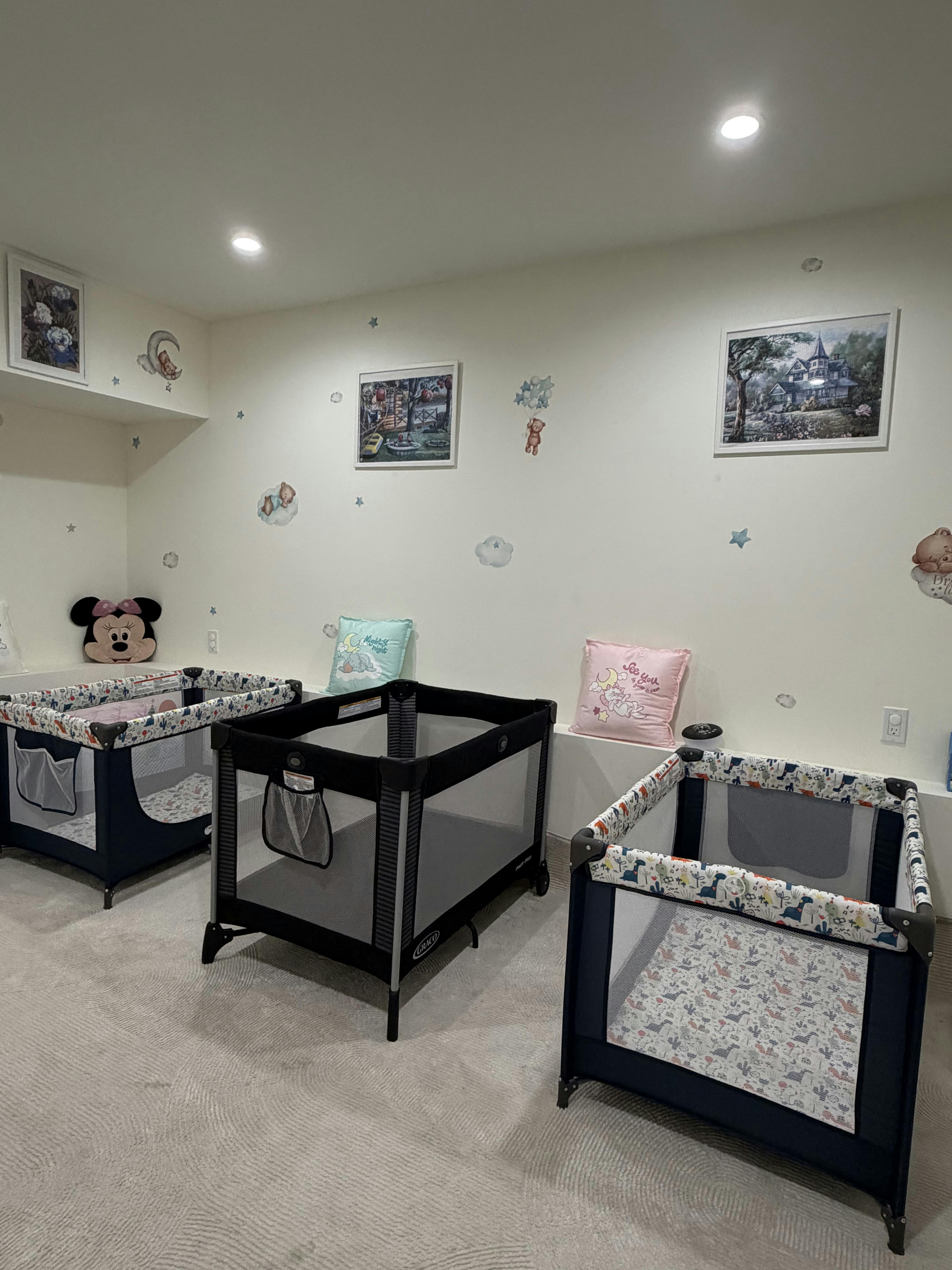 Three playpens in a room with cartoon wall decals and pictures