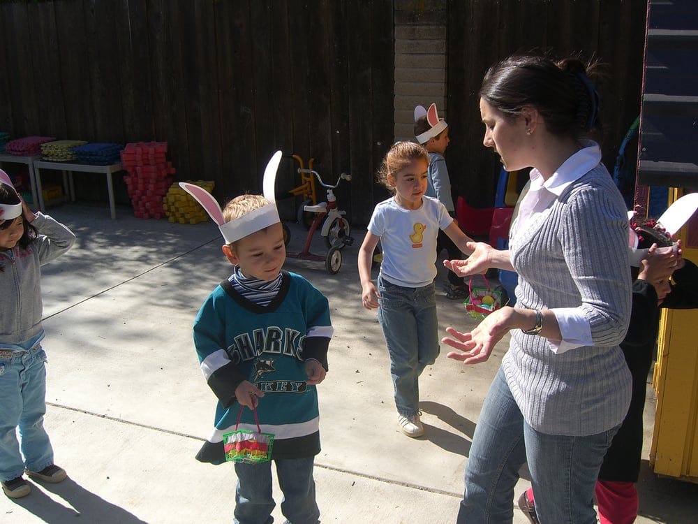 Adult speaking to children wearing bunny ears, one holding a basket