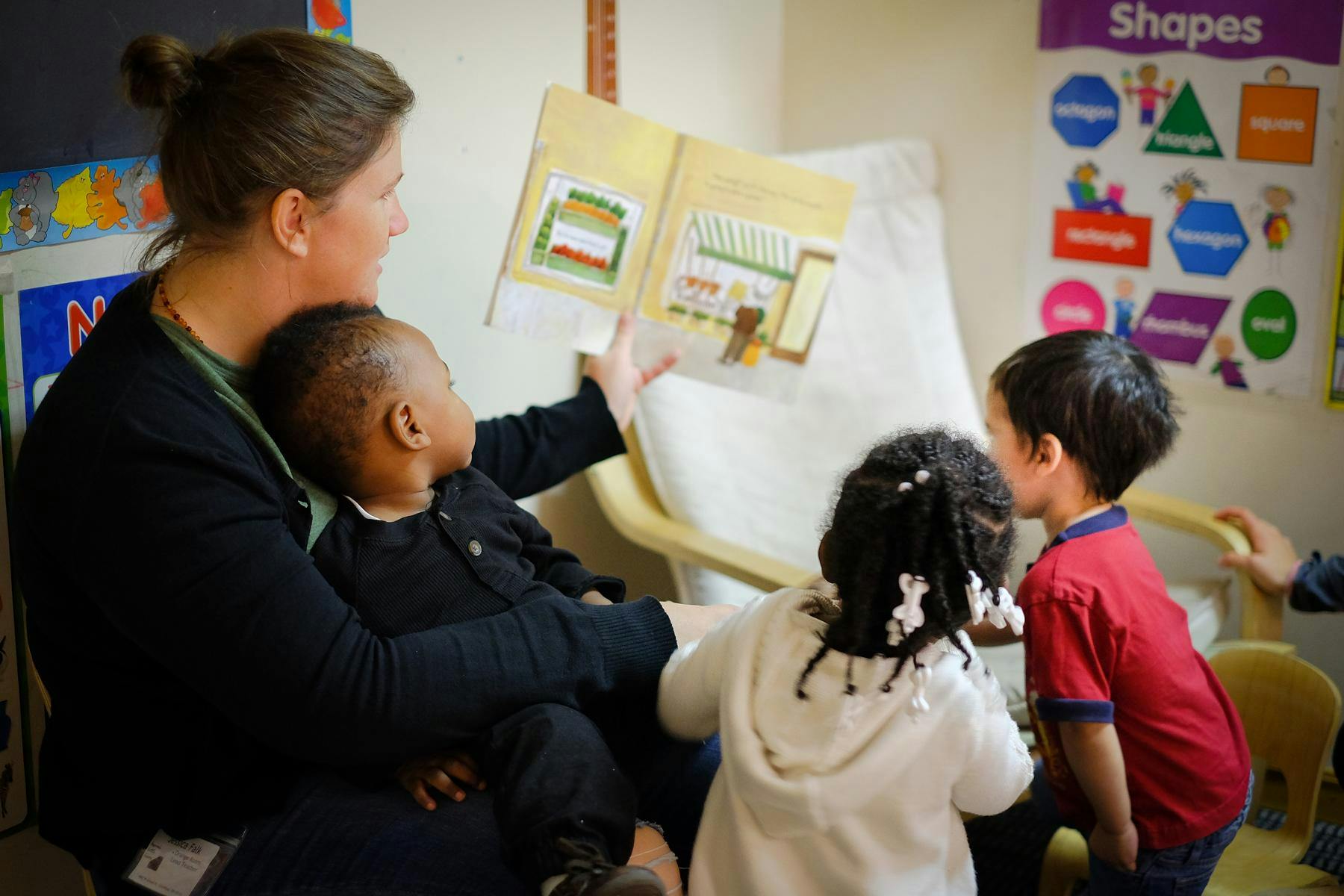 Person reading a book to three children in a classroom