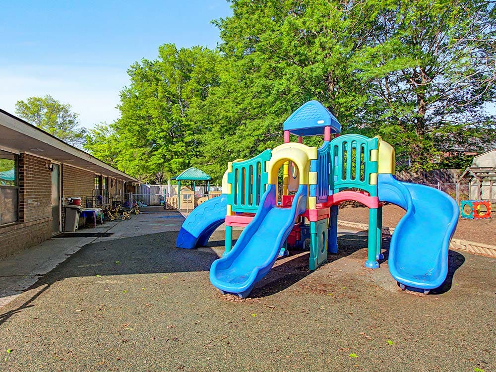 Colorful playground structure with slides on a padded surface next to a building