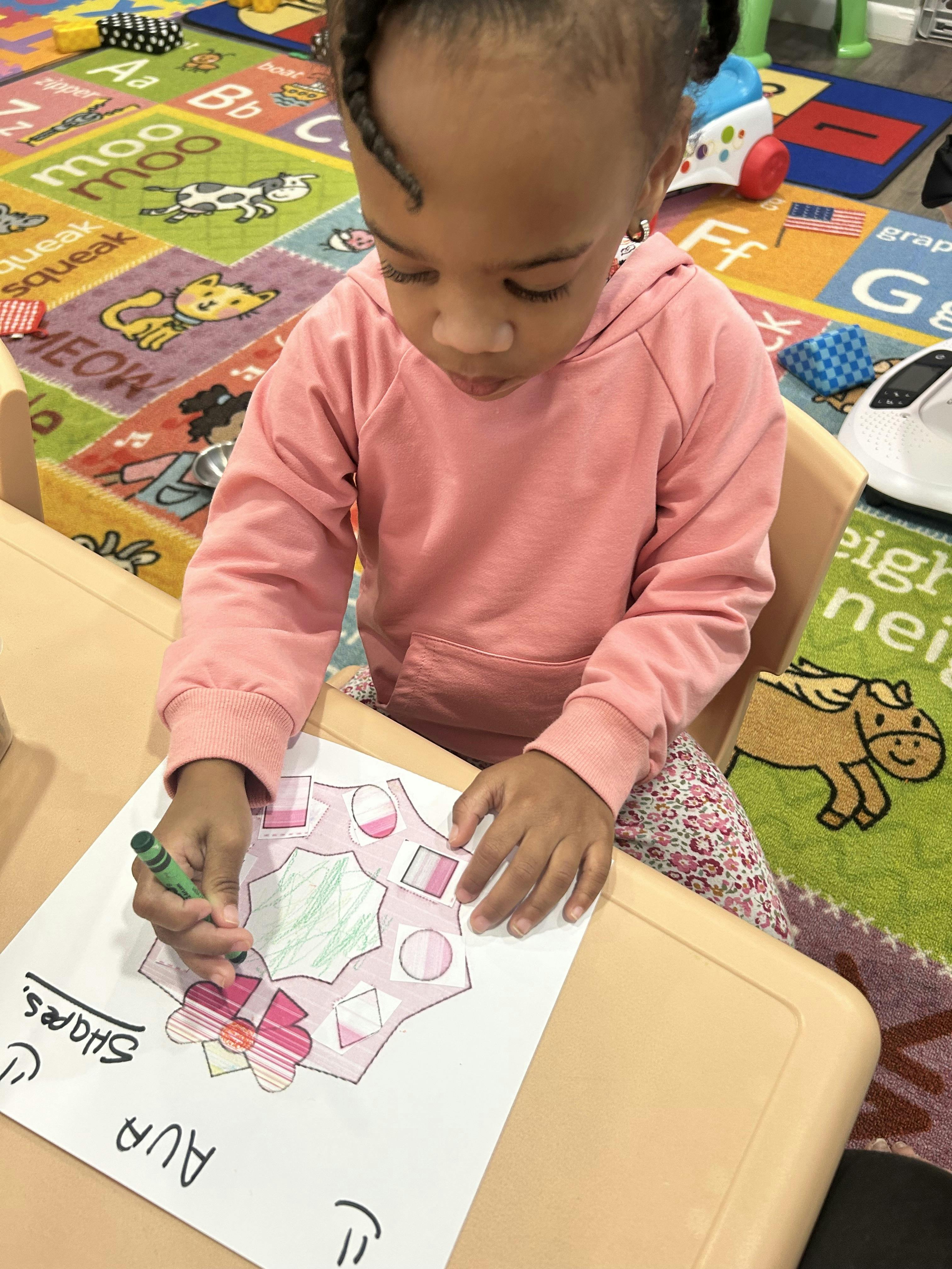 child coloring a paper with various shapes with a green crayon