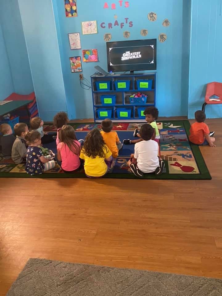 Children sitting on a rug watching a television in a classroom
