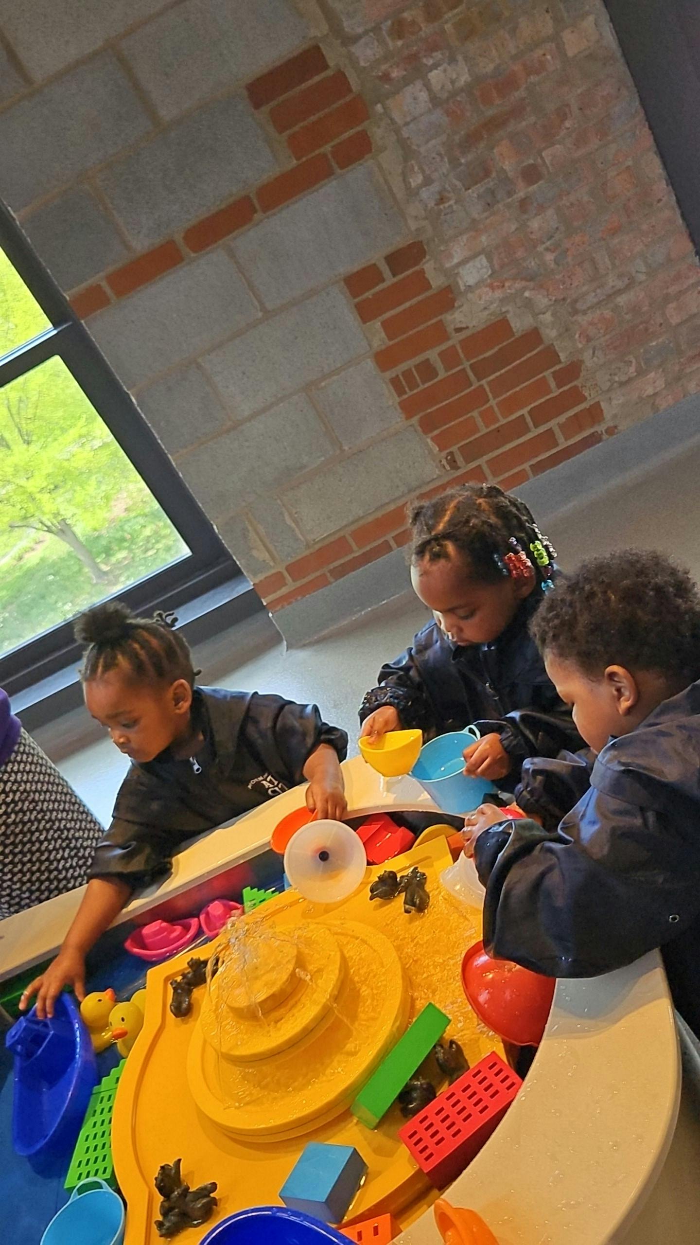 Three children playing at a water table with toys