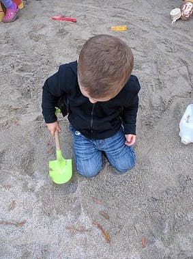 Child kneeling in sand with a green shovel