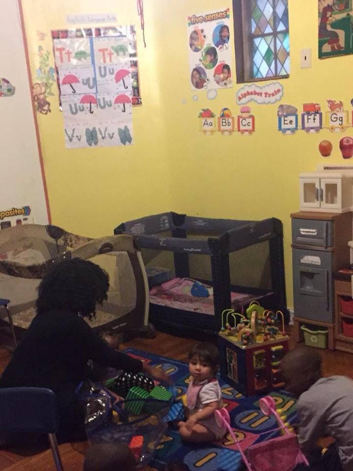 Person and two children playing on a rug in a room with cribs
