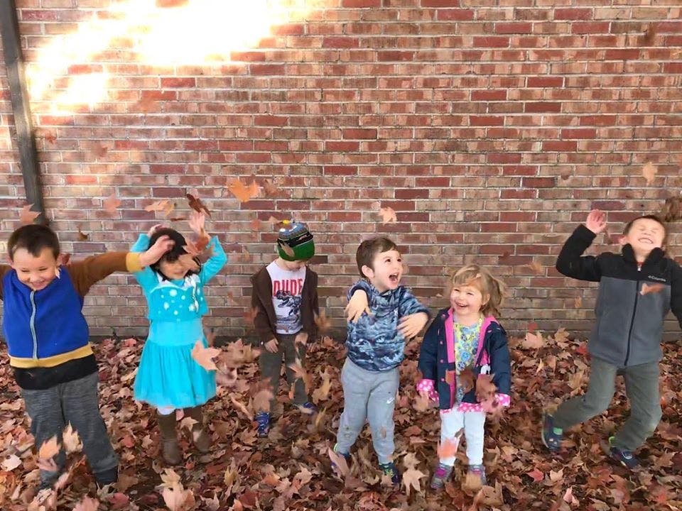 Children playing in fallen leaves in front of a brick wall
