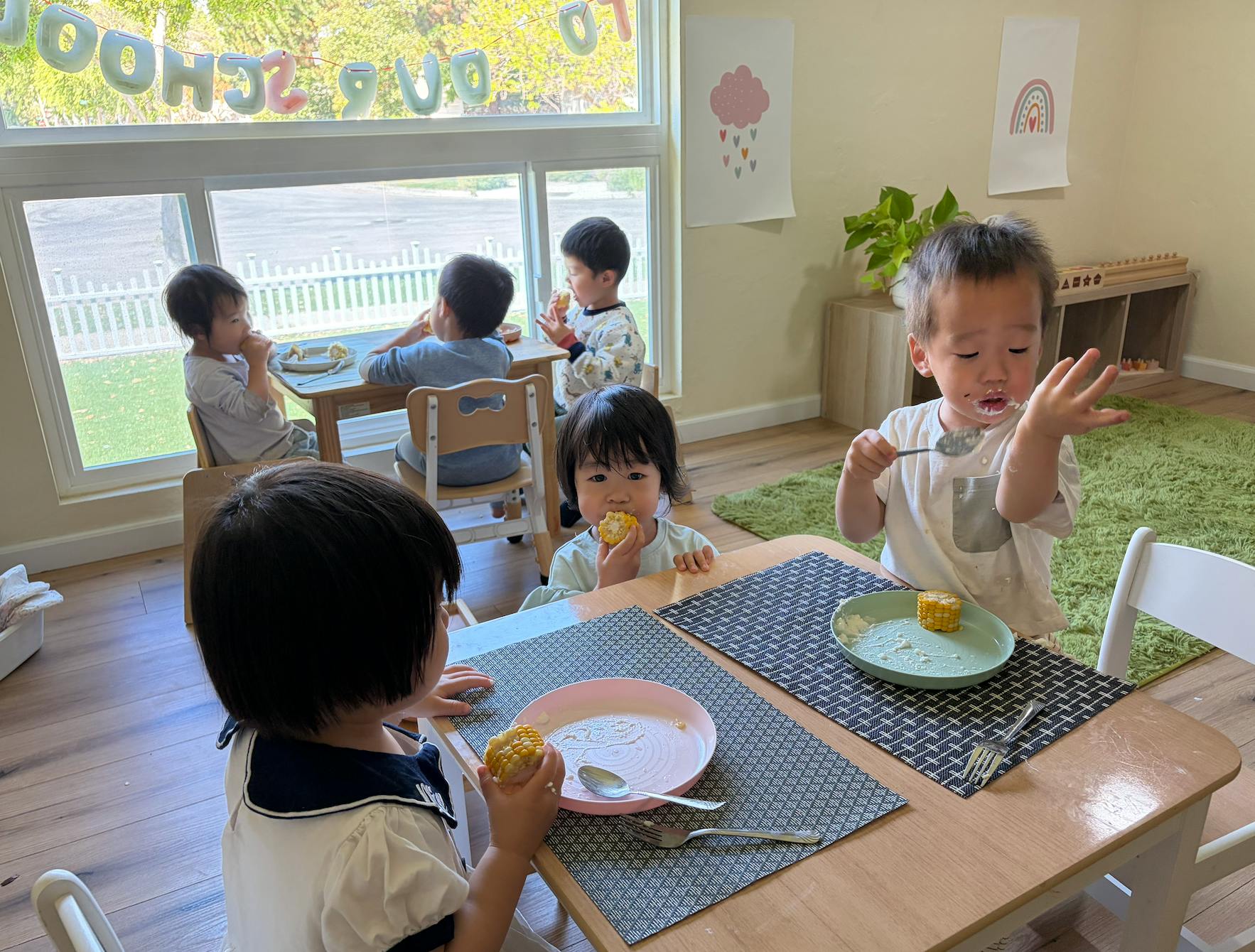 Children eating corn on the cob at a low table in a classroom