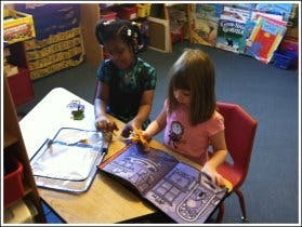 Two children looking at a book at a table