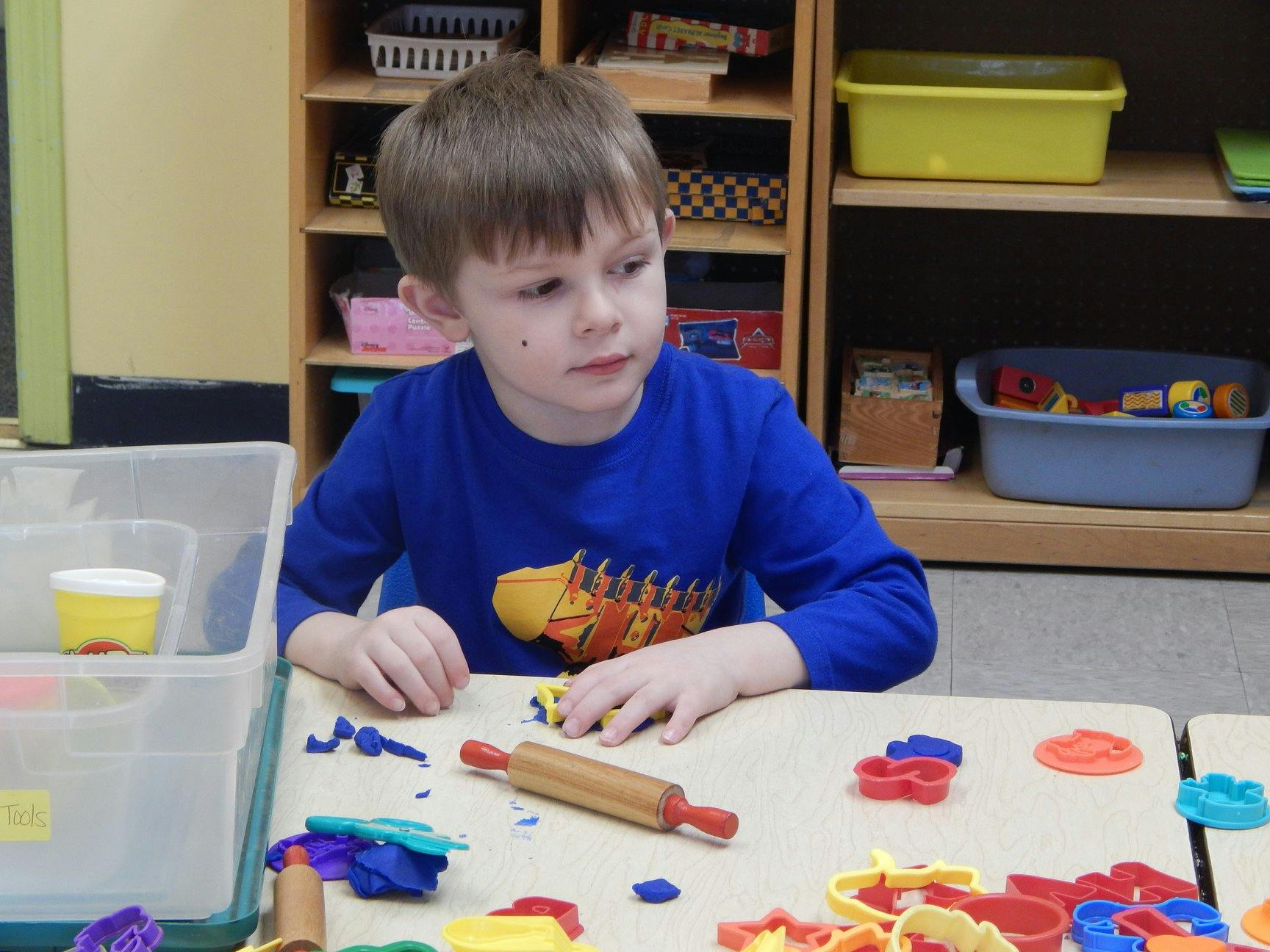 Child playing with modeling clay and a rolling pin at a table