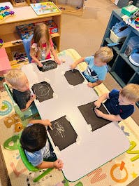 Four children and one adult at a table with art supplies
