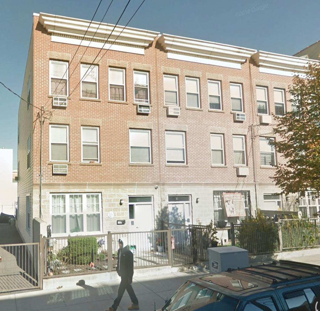 Person walking past a brick apartment building with a fence
